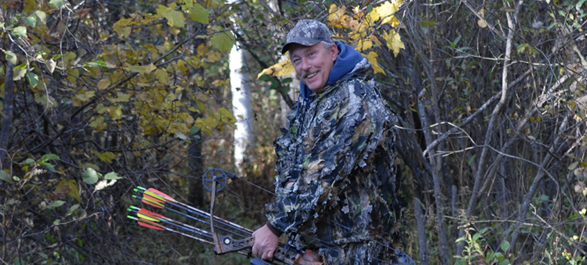 Adult man in camouflage holds a bow for